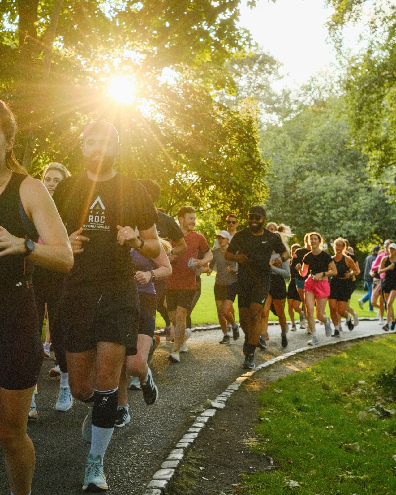 Runners on a park path with the sun shining through the trees.
