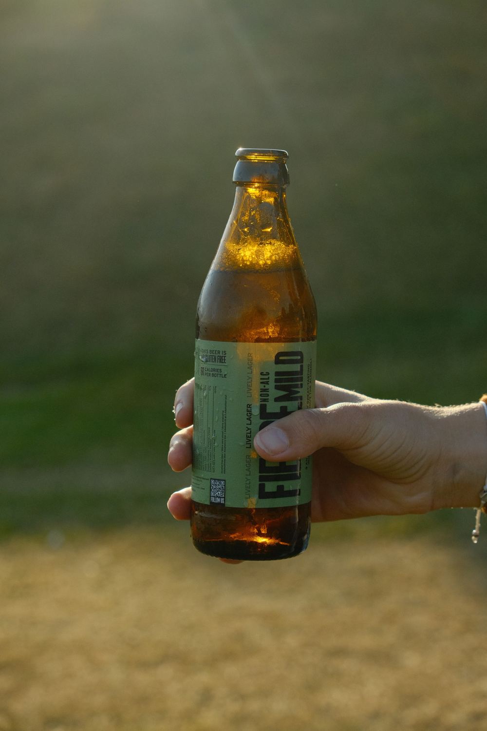 A bottle of Fierce Mild Lively Lager held up in evening sun.
